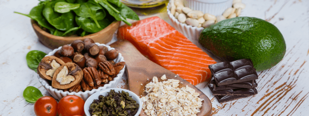 Anti-inflammatory nutrition foods featuring wild salmon, avocado, spinach, nuts, seeds, oats, tomatoes, olive oil, and dark chocolate on a white rustic surface.